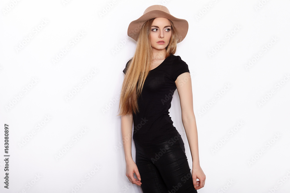 Young beautiful fashion model in women black t-shirt trendy hat black torn jeans posing in studio against white background Young beautiful fashion model in women black t-shirt trendy hat black torn jeans posing in studio against white background