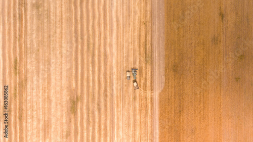 Aerial shot of an agricultural wheat field, a combine harvester  and a truck in Europe