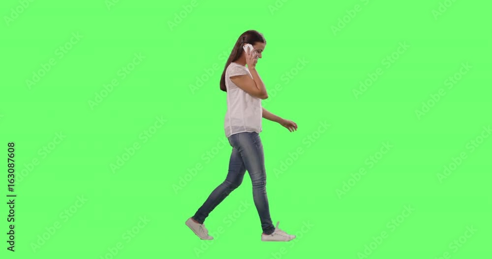 Casual Young Brunette Girl is Walking and Talking on the Smartphone on a Mock-up Green Screen in the Background. Casual Young Brunette Girl is Walking and Talking on the Smartphone on a Mock-up Green Screen in the Background.