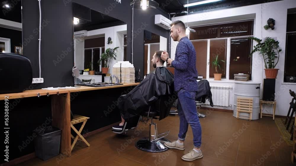 Side view of master combing hair to male customer in barber shop Side view of master combing hair to male customer in barber shop