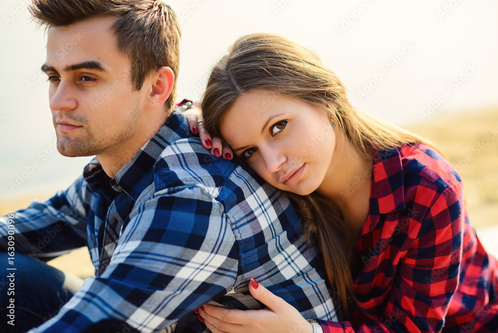 Stylish young couple in shirts and jeans while walking on the shore of a lake. Beautiful charming girl hugs her handsome boyfriend. Close up portrait. Stylish young couple in shirts and jeans while walking on the shore of a lake. Beautiful charming girl hugs her handsome boyfriend. Close up portrait.