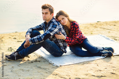 Stylish young couple in shirts and jeans while walking on the shore of a lake. Beautiful charming girl hugs her handsome boyfriend.