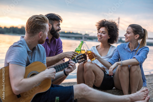 Group of friends with guitar having fun on the beach. Soft focus, high ISO, grainy image. © GutesaMilos