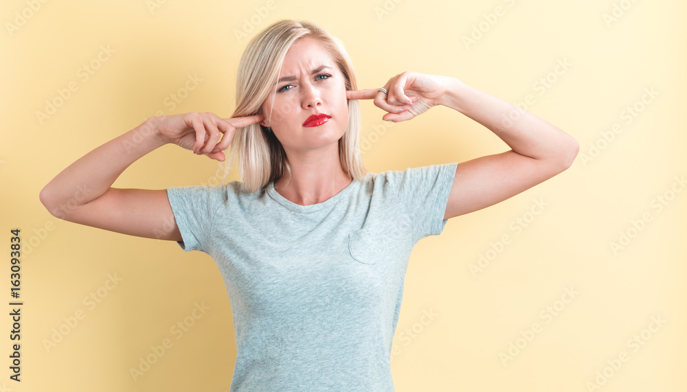 Young woman blocking her ears on a yellow background Young woman blocking her ears on a yellow background