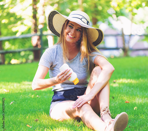 Young woman a bottle of sunblock outside on a summer day