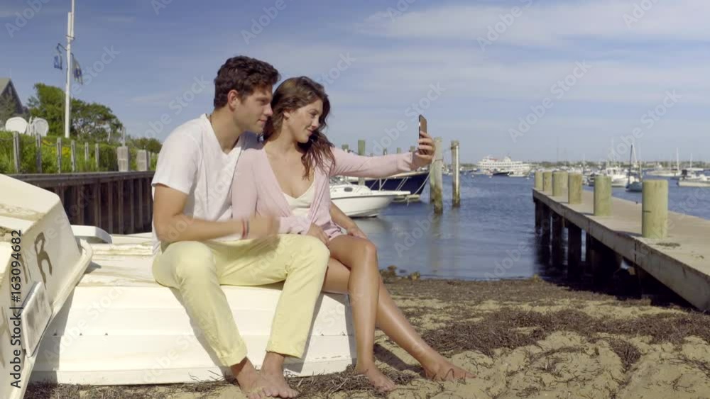 Attractive Couple Pose For Selfies, Sitting On A Boat, At Beach