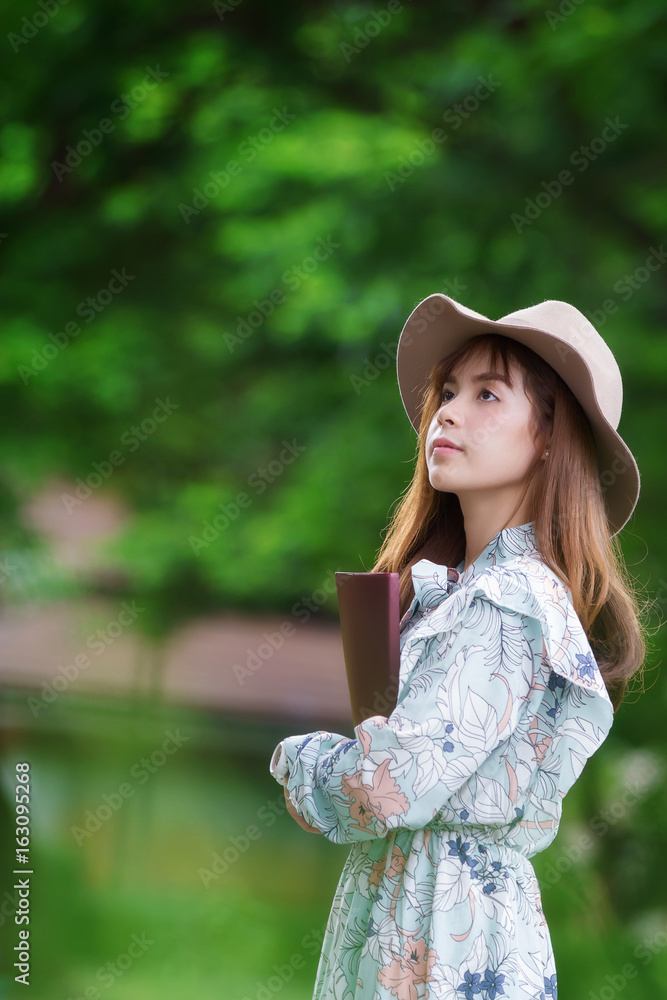 Obraz premium Beautiful asian woman holding book and relaxing in park