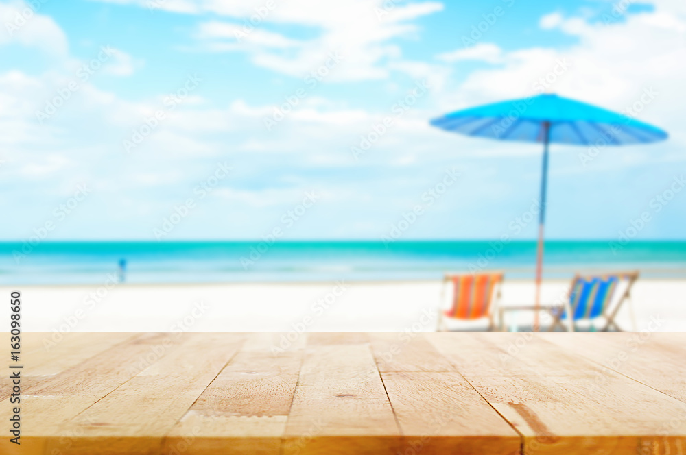 Wood table top on blur beach background with beach chairs and parasol Wood table top on blur beach background with beach chairs and parasol