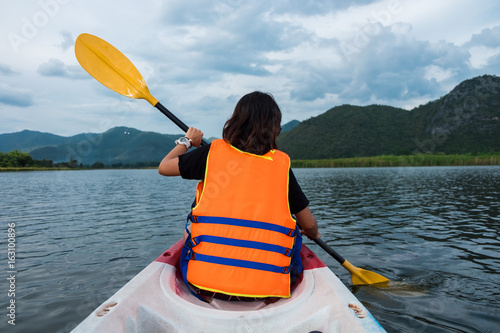 back view. woman wearing life jacket sitting relax. her paddle around sea. have sea and mountain are background. image for nature,travel, portrait concept