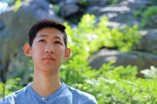 Close up portrait of young attractive asian american man standing next to scenic mountain forest background