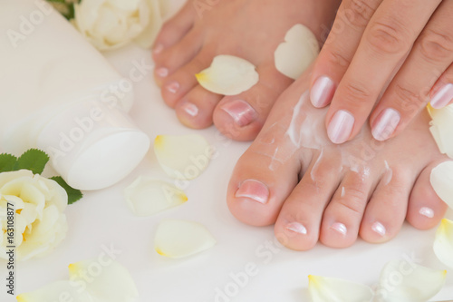 Young woman s feet with moisturizing cream. Smooth skin. Spring and summer atmosphere with fresh and fragrant white roses.