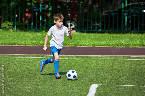 Boy football player running with ball on green lawn