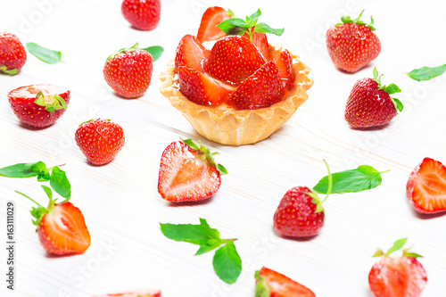 Fototapeta Naklejka Na Ścianę i Meble -  Tasty cake basket with strawberries and cream on a white wooden background with berries and leaves of fresh mint