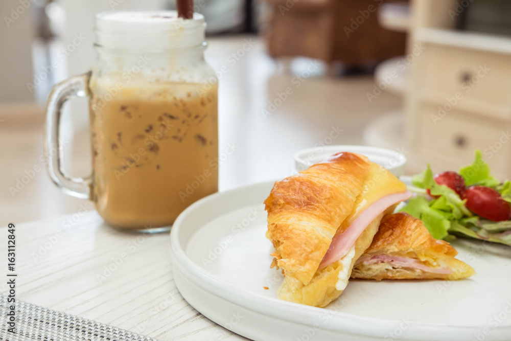 Croissant ham cheese with vegetable and ice coffee in background Croissant ham cheese with vegetable and ice coffee in background