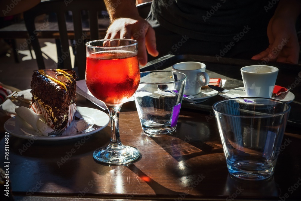 Table, light glass of red beverage, coffe, cake, water, glass, hand. Dark Table, light glass of red beverage, coffe, cake, water, glass, hand. Dark