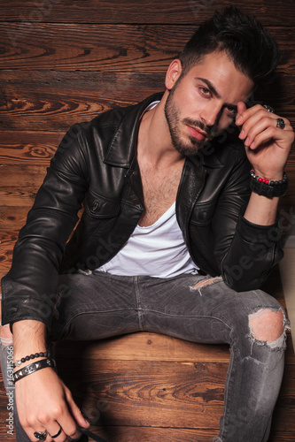 man in leather jacket and jeans sitting on wooden background © Viorel Sima