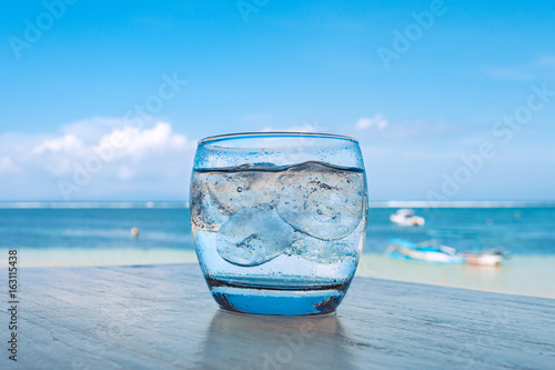 Cool drink on table with tropical beach setting behind.