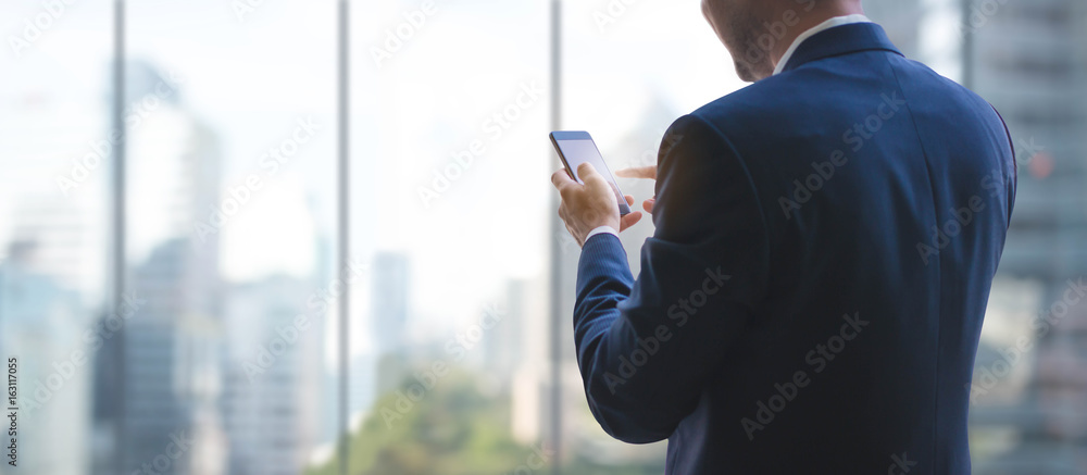 Business man using smart phone on window with city building background and copy space.