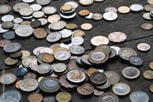 A pile of coins from different countries on a wooden table