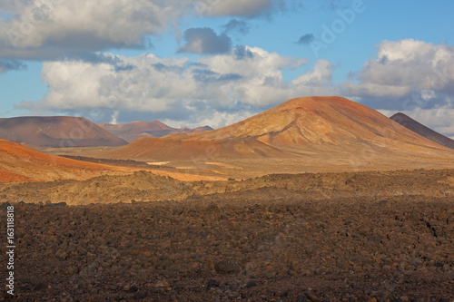 Lifeless red volcanic terrain illuminated by sunlight and shadow in the foreground on Lanzarote island, Canary Islands, Spain