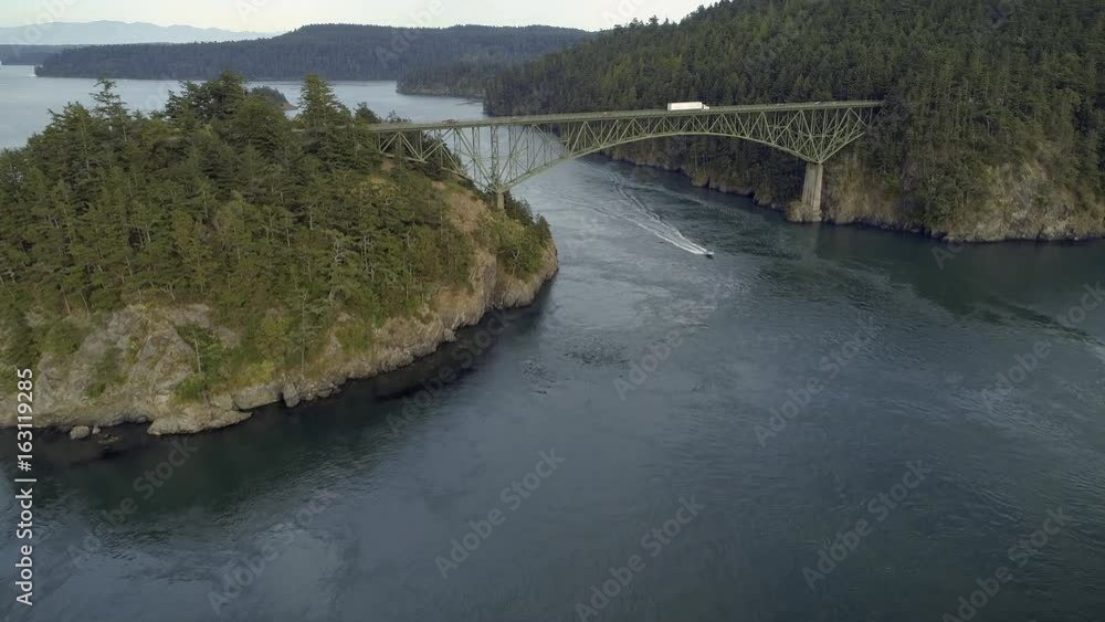 Helicopter Filming Boat Cruising Under Large Pacific Northwest Bridge with Truck Delivering Package Driving Across Helicopter Filming Boat Cruising Under Large Pacific Northwest Bridge with Truck Delivering Package Driving Across