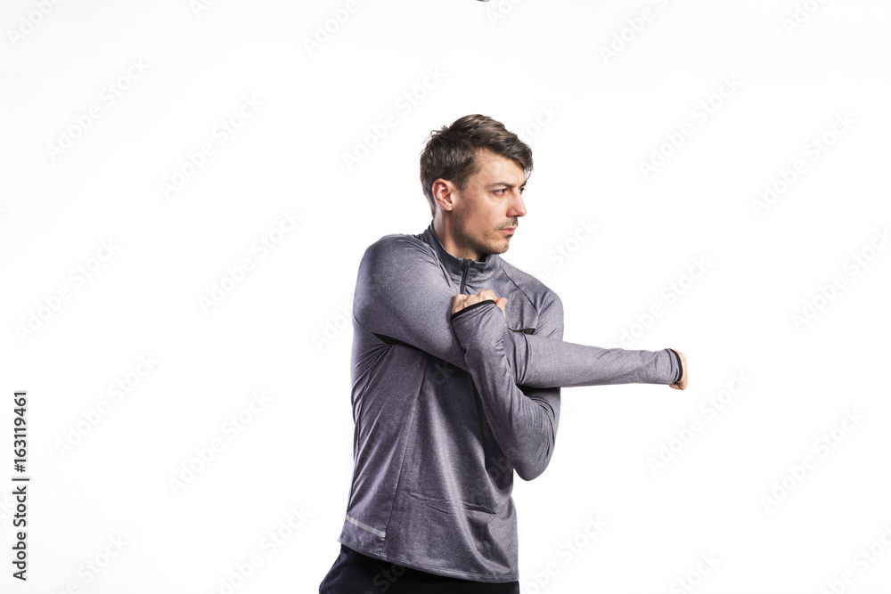 Fit man in gray sweatshirt stretching arms, studio shot. Fit man in gray sweatshirt stretching arms, studio shot.