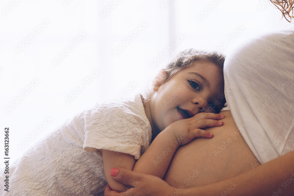 Happy kid girl hugging pregnant mother's belly Happy kid girl hugging pregnant mother's belly
