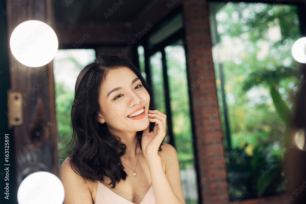 Naklejka premium Pretty happy asian woman watching on herself in a big mirror at home.