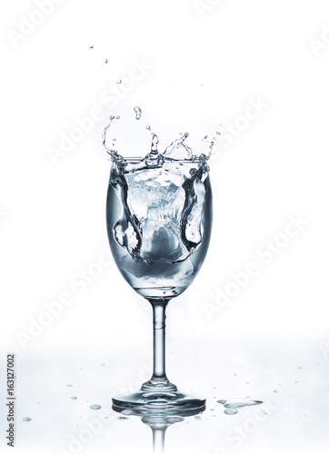 Water splash with ice in glass on white