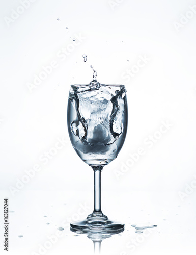 Water splash with ice in glass on white