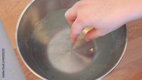 A woman puts gelatin sheets into a steel bowl with water - closeup from above photo