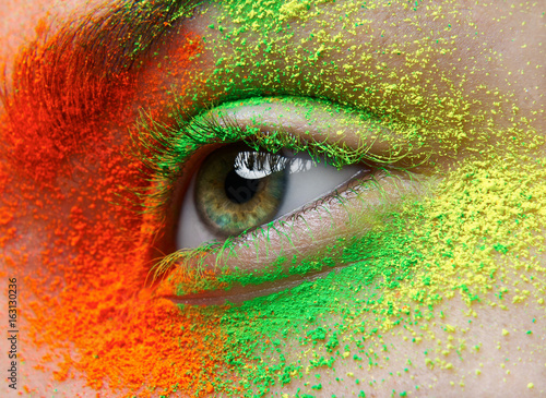 Macro and close-up creative make-up theme: beautiful female eye with orange, green and yellow pigment, retouched photo