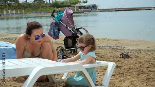 Mom and daughter, 4-5 year old girl, on the beach. The girl is drawing. photo