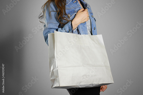 The girl in the blue denim shirt holding blank clean paper bag. Ready for your design. Closeup. Isolated
