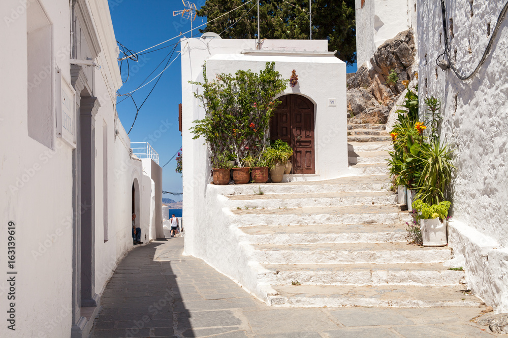 Narrow streets and typical Greek buildings in the city of Lindos on the island of Rhodes. Residential buildings at the foot of the mountain on which the Acropolis is located.