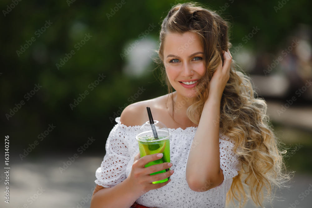 Portrait of a young beautiful attractive woman outdoors in the summer with a glass of ice-cold juice or drink. Pretty girl outside with fresh mojito Portrait of a young beautiful attractive woman outdoors in the summer with a glass of ice-cold juice or drink. Pretty girl outside with fresh mojito