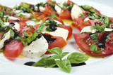 Caprese salad. Sliced tomatoes, mozzarella and shredded basil, poured with oil and vinegar, sprinkled with salt and colour pepper laying on white plate.