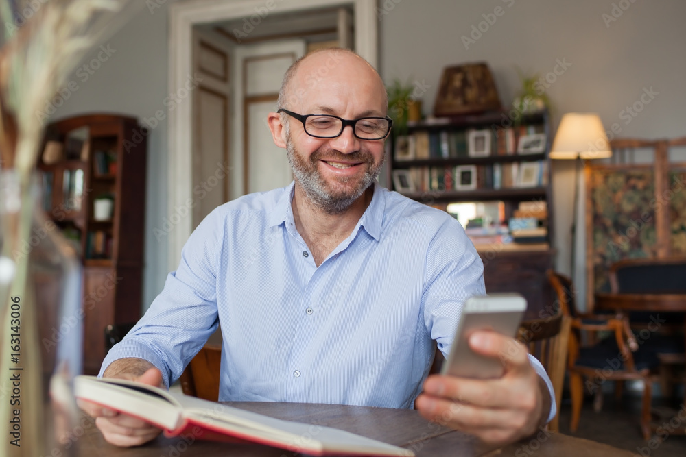 Man reading book indoor and using phone
