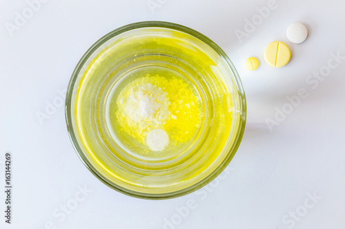 Medicine tablets slow dissolving in glass water and three tablets outside in light beam on white background.