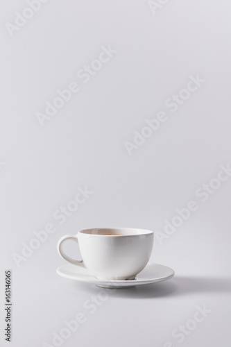 white cup with aromatic coffee on saucer isolated on grey with copy space