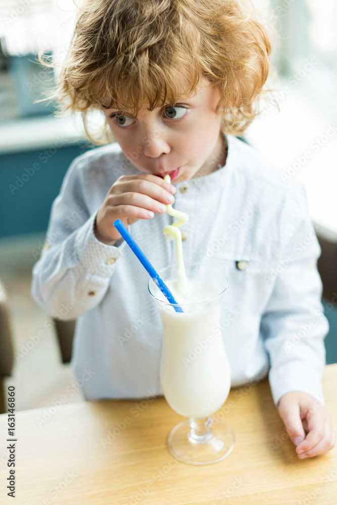 portrait of little boy drinking delicious milkshake from straw in cafe portrait of little boy drinking delicious milkshake from straw in cafe