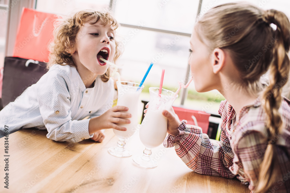 adorable happy little children drinking milkshakes with straws in cafe adorable happy little children drinking milkshakes with straws in cafe