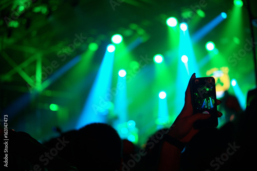 Human hand with smartphone recording concert in crowd