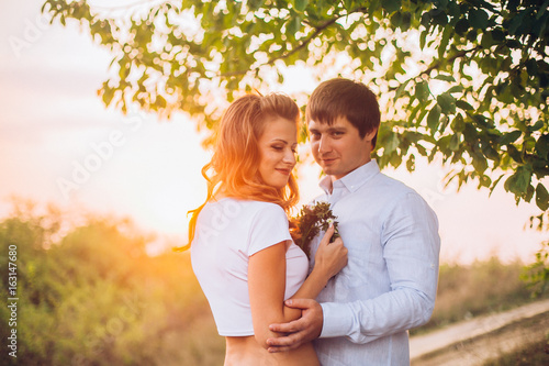 Young kissing couple under big tree at sunset