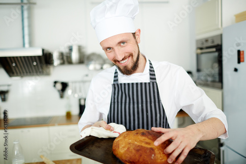 Happy baker taking hot bread from tray