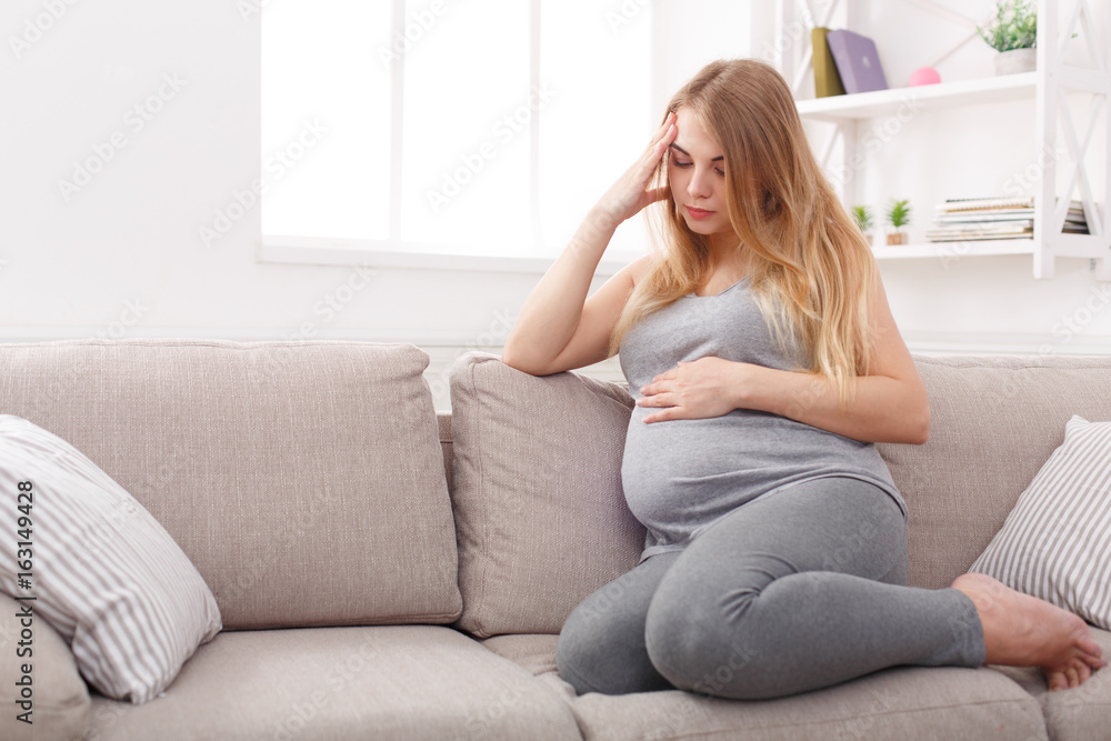 Thoughtful pregnant woman sitting on sofa Thoughtful pregnant woman sitting on sofa