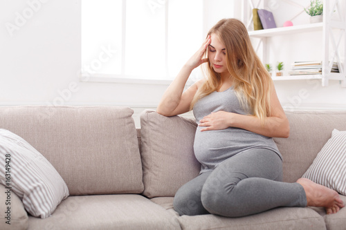 Thoughtful pregnant woman sitting on sofa