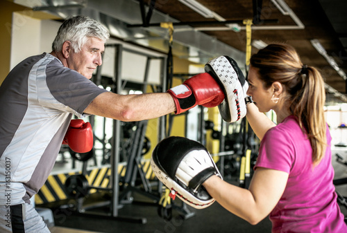 Older man boxing in gym. Senior man with personal trainer.