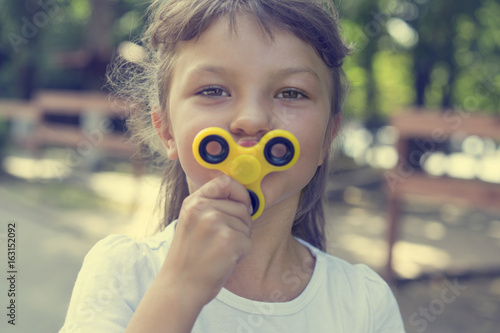 A young beautiful girl in a white T-shirt attached to the face a yellow spinner on the street photo