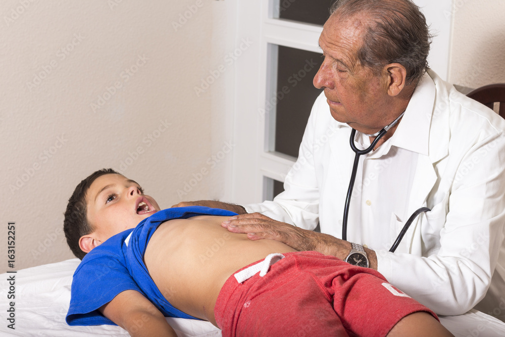 Obraz premium Senior male doctor with stethoscope examining a young boy child